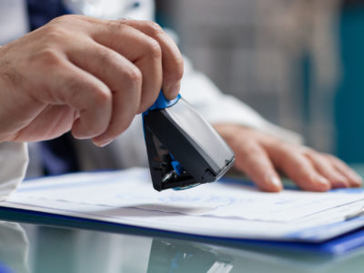 Doctor holding medical stamp to put on prescription paper at health care exam. Hand of physician putting seal on checkup report, giving medicine to patient at consultation. Close up